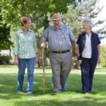 Due donne anziane e un uomo anziano affetti da demenza camminano in un prato verde