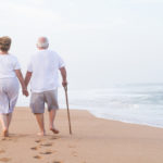coppia di anziani di spalle camminano in vacanza sulla spiaggia in riva al mare